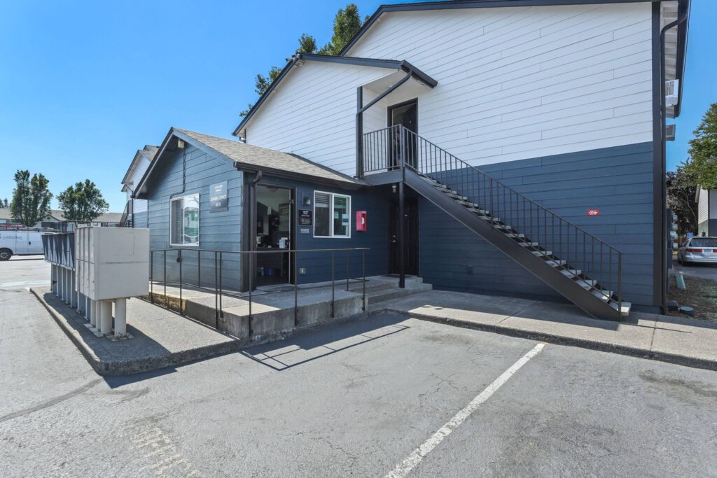 A two-story building with dark blue and white siding, featuring an external staircase and open office space.